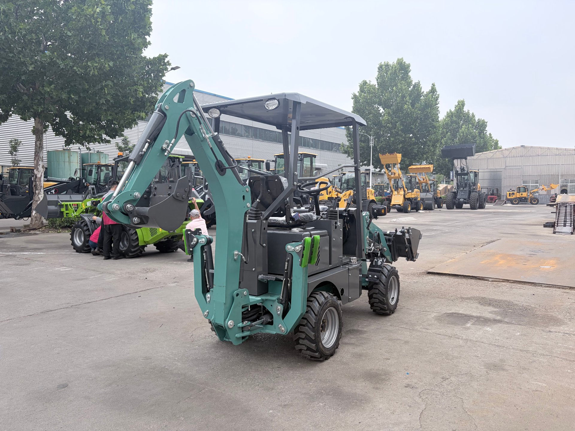 Green AOLITE mini backhoe loader parked in the factory yard with a row of machines behind it