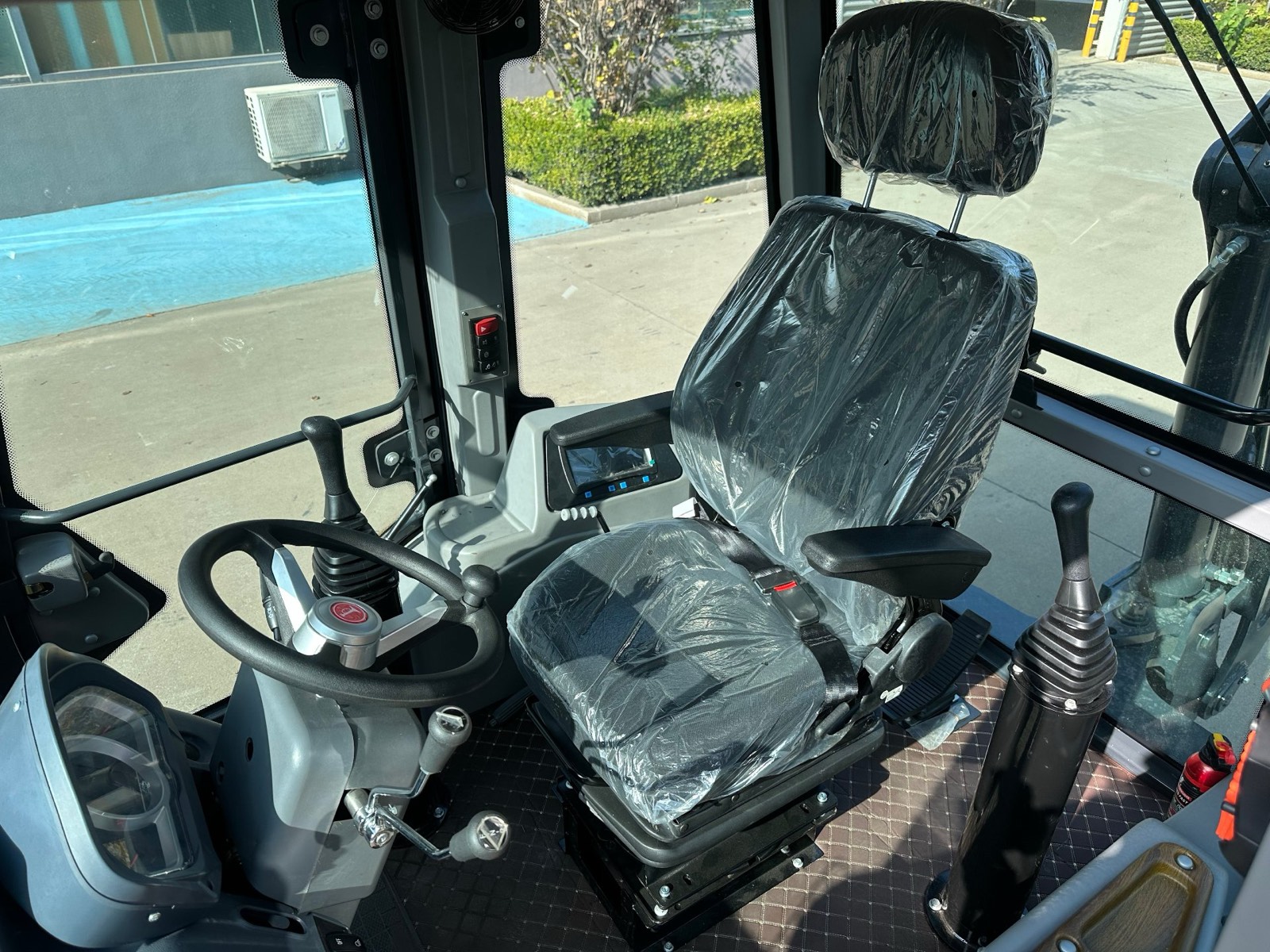 Inside the cab of a new AOLITE backhoe loader before delivery, seat still wrapped in protective film