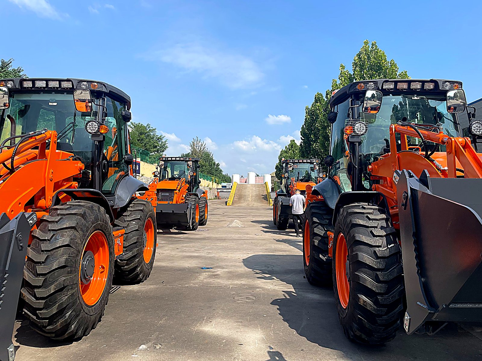Rows of finished backhoe loaders parked in the factory yard waiting for shipping, seen from ground level