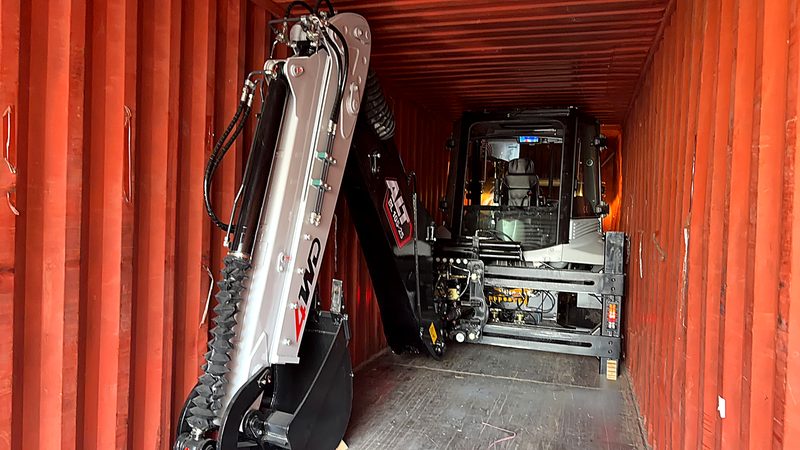 Backhoe loader inside a red shipping container, ready for export