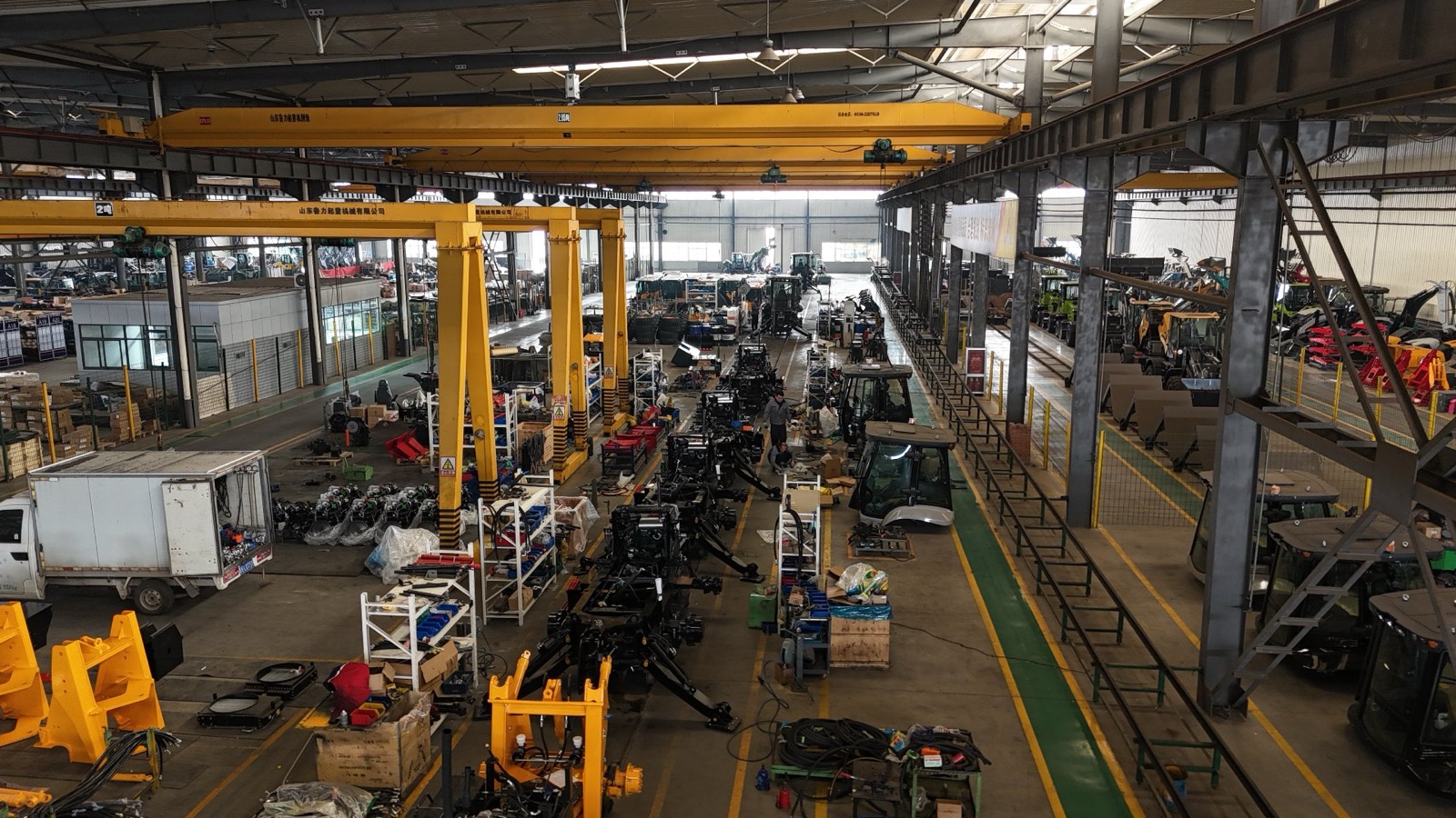 The AOLITE assembly hall seen from the overhead walkway, with backhoe loader chassis in sequence along the production line