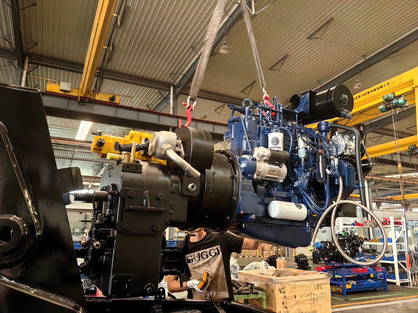An engine and transmission assembly being lowered by crane onto a backhoe loader chassis on the AOLITE production line