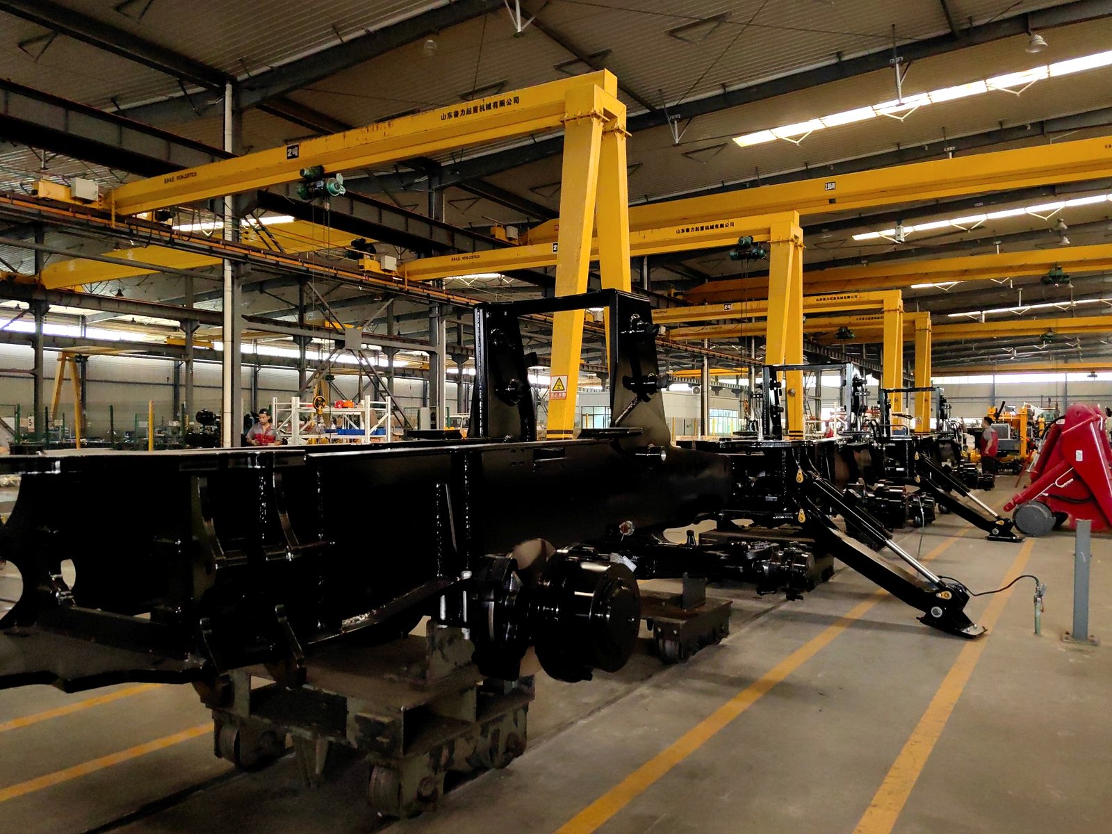 Chassis frames for backhoe loaders on the assembly line inside the AOLITE factory under overhead cranes